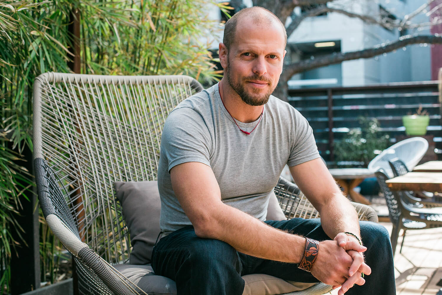Tim Ferriss in jeans and a t-shirt sitting forward on a patio chair.